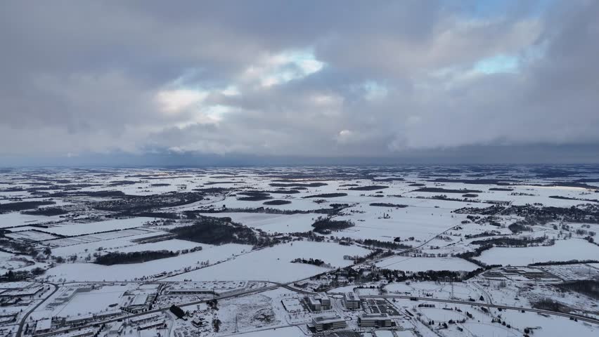 A drone footage of snow-covered district under dramatic cloudy sky with farmlands in the background in Waterloo, Ontario, Canada