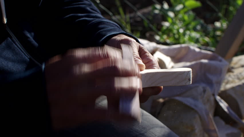 A skilled artisan meticulously shapes wood using traditional techniques in a peaceful outdoor location. The bright sun illuminates the natural surroundings, enhancing the experience.