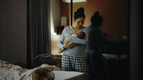 Authentic footage of a mother in pajamas at night trying to put her newborn baby to sleep in her arms. The mother is very tired and yawns and cuddles her baby in the bedroom - Powered by Shutterstock - Get 15% off with code: PIKWIZARD15