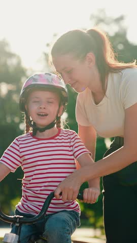 Elder sister teaches kid girl to ride bike park. Child cyclist with mom, nature. Sport family, little girl in helmet together with her mother learns to ride bicycle outdoors in summer. Family weekend
