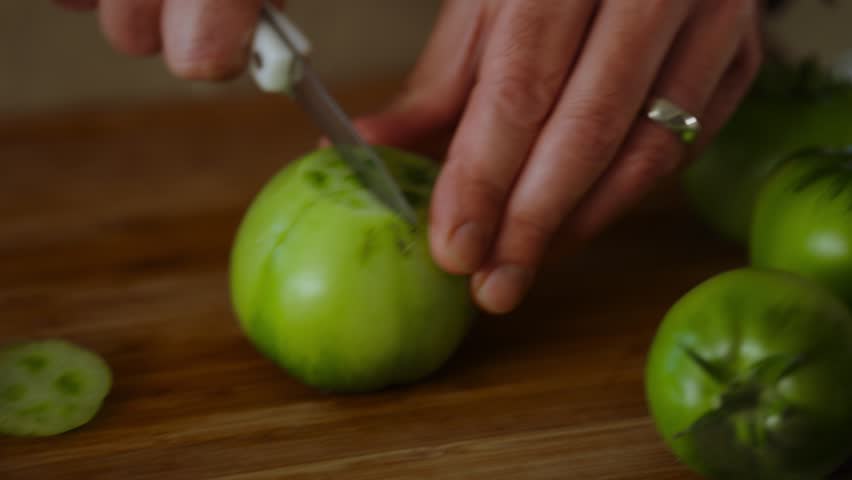 Cutting of fresh green tomatoes by a male chef on chopping board.