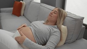 Pregnant woman relaxing on a sofa in a cozy living room with her hand on her belly, capturing a serene moment of expecting mother in a comfortable home setting. - Powered by Shutterstock - Get 15% off with code: PIKWIZARD15
