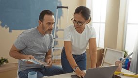 Middle-aged hispanic couple planning home renovation in living room with laptop and color swatches, showing love and teamwork in cozy setting. - Powered by Shutterstock - Get 15% off with code: PIKWIZARD15