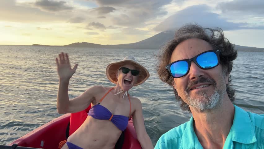 A mature man and woman smile joyfully while kayaking at dusk on Lake Nicaragua, with the stunning Concepcion Volcano in the background. Selfie in Central America.