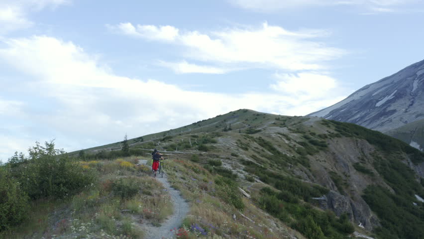Two friends with mountainbikes walking uphill on mountain ridge trail, Mount St. Helens, aerial