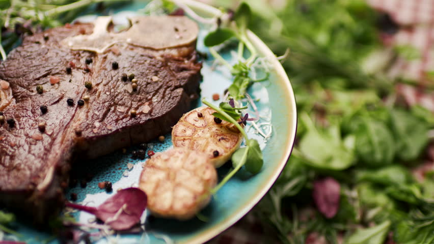 Grilled T-Bone Steak Rotating on Table with Fresh Greenery