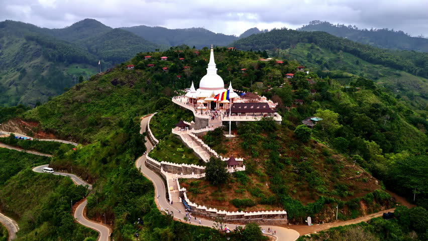 Drone aerial landscape of Mahamevnawa Buddhism monastery sanctuary temple buildings with Buddhist flag on mountaintop of forest valley Kandy Ella Sri Lanka religion spirituality tourism sacred site