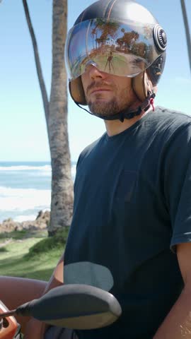 Man wearing moto helmet sitting near ocean on a sunny day. 