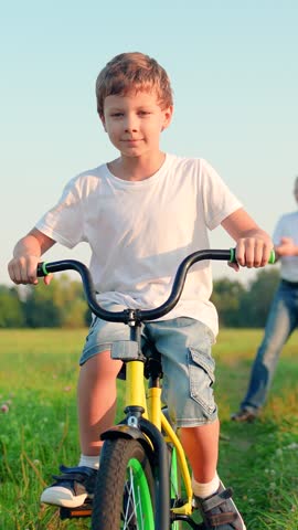 Sports lifestyle of child, boy cyclist play. Child boy rides bike in park on green grass. Happy family in park. Child's feet are pedaling. Boy rides bike in summer, pedaling. Childhood dream to travel