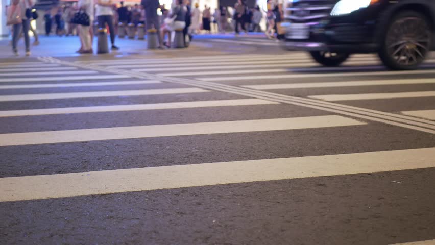 selective focusing low anngle view at zebra crossing area in downtown Taipei capital city Taiwan in night time while cars and mmotorike moving fast on green light, pedestrian waiting to cross stret