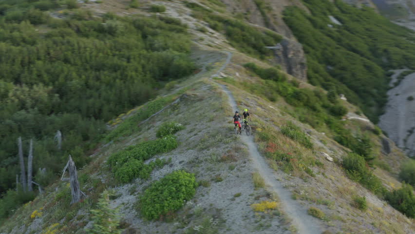 Two mountainbikers standing on mountain trail ridge at foothills of Mount St. Helens, orbit shot