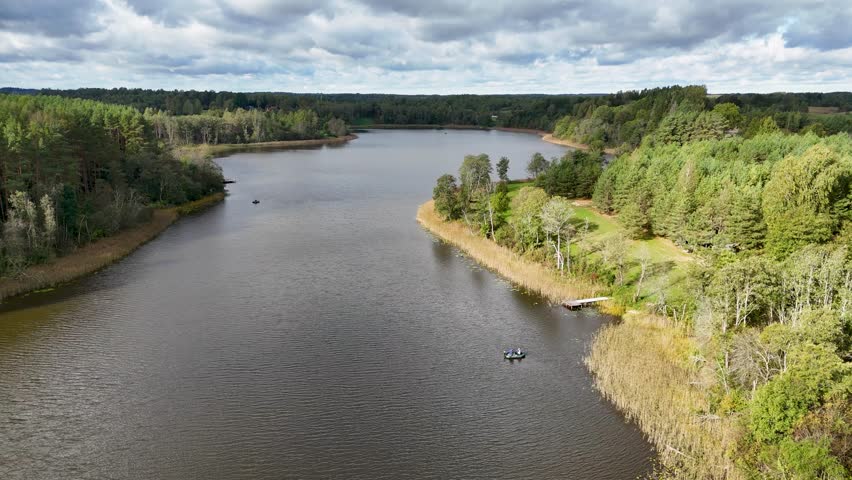 A scenic aerial view of a serene lake surrounded by lush green forests under a cloudy sky. Two small boats are visible on the water, adding a sense of tranquility to the landscape.