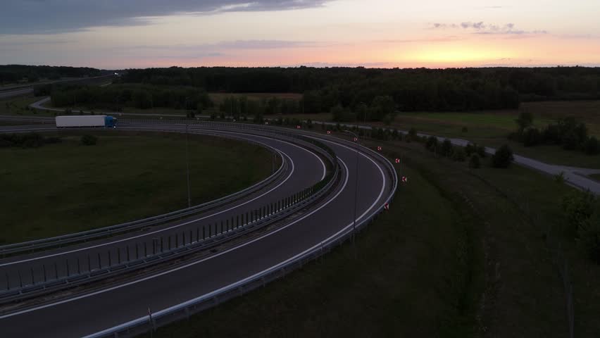 Drone shot of a truck navigating a curved road at dusk, with highway guardrails in view.
