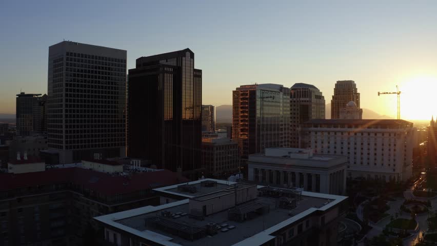 Aerial drone shot of downtown Salt Lake City, dollying in over downtown. Skyscrapers, apartments, and offices line the street glowing under a golden-orange autumn sunset.