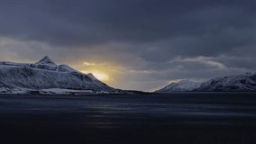 The setting sun appears from behind the clouds above the snow-covered mountains surrounding Norwegian fjord. Lofoten Islands, Norway. - Powered by Shutterstock - Get 15% off with code: PIKWIZARD15