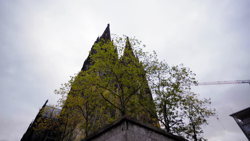The iconic Cologne Cathedral spires partially hidden by vibrant autumn foliage, highlighting the interplay between nature and historic architecture in Cologne, Germany