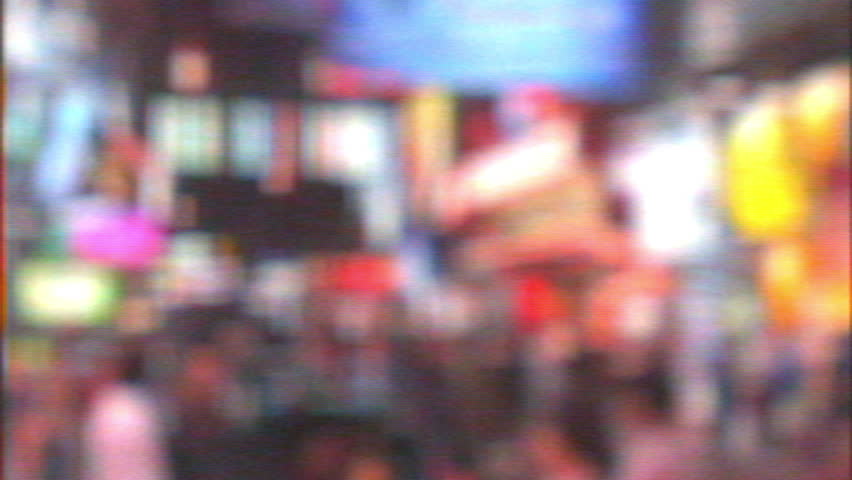 A heavily blurred VHS video captures a bustling nighttime street scene in South Korea, with large crowds moving amidst bright lights and a backdrop of buildings and neon-lit shops