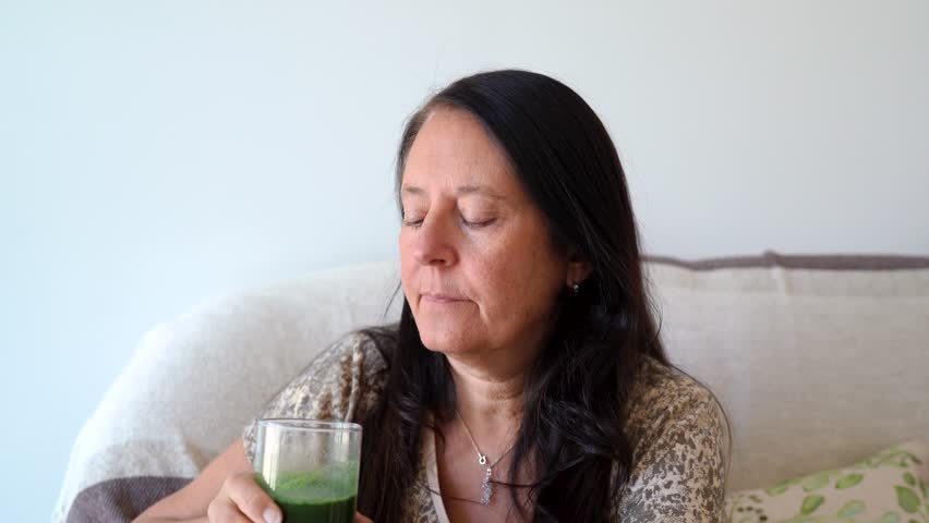 Middle-age woman drinking natural green juice with spirulina powder on it.