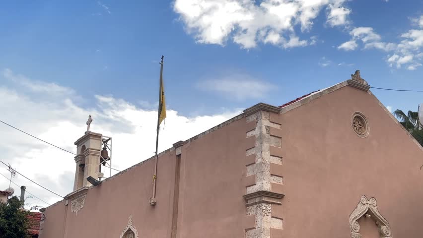 Historic church with beige walls and Greek flag in Hersonissos, Crete, Greece