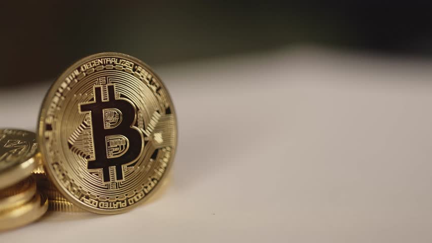 batch of physical bitcoins in bright light, shining gold. Display BTC establishment pan shot, coin in depth of field on white blurry background