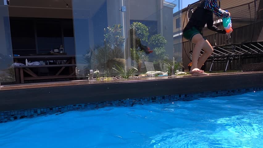A young boy spins around while jumping into a pool with a water gun into fast paced battle with his friends. Point of view.
