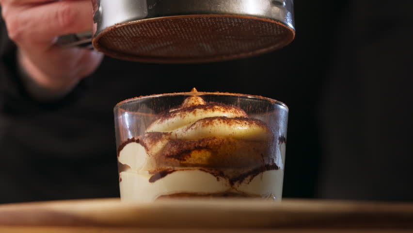 Sifting Cocoa Powder Over Tiramisu Dessert. - closeup shot
