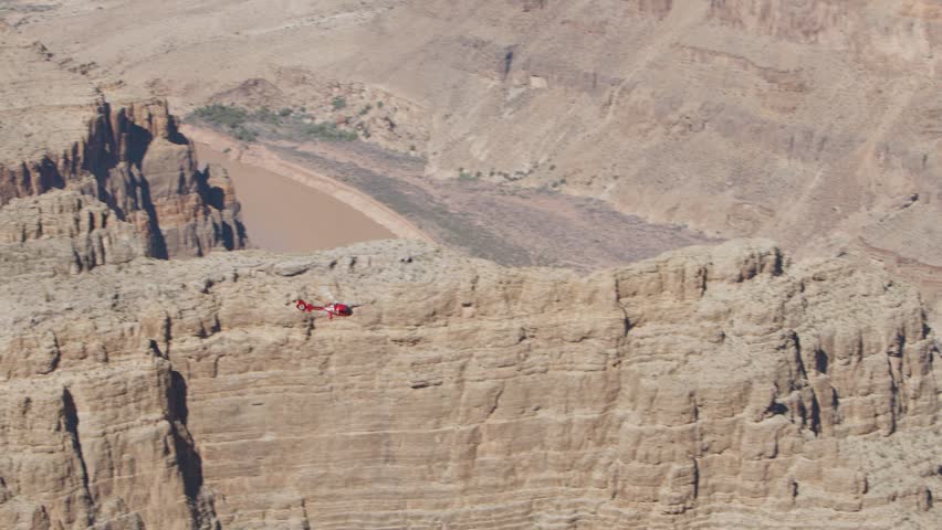 A helicopter soars over a large canyon and disappears behind it.