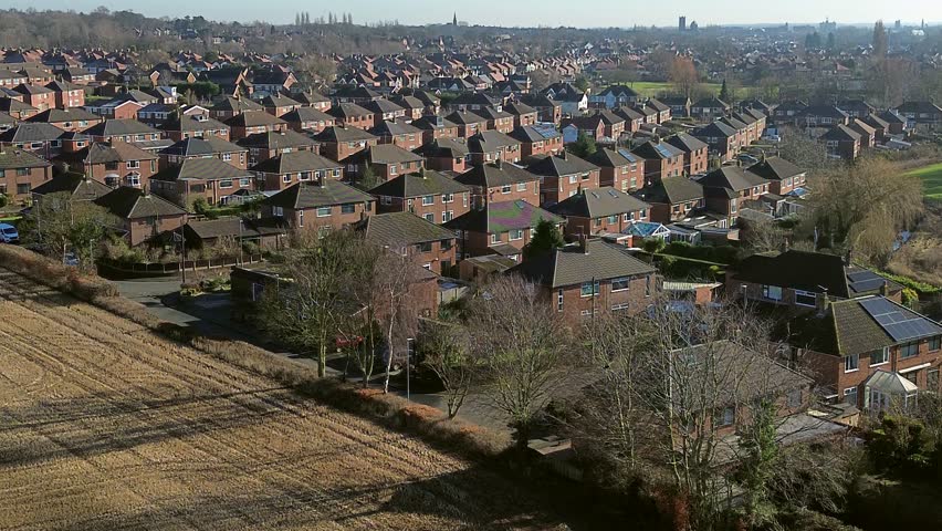 Rows of identical British town houses suburb aerial rising view alongside idyllic farmland