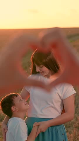 Father Looking through Heart symbol made by fingers at happy family. Mom hugs her little daughter, dad looks at them through hand heart sign in park. Love for family for child, mother. Mom, dad, child