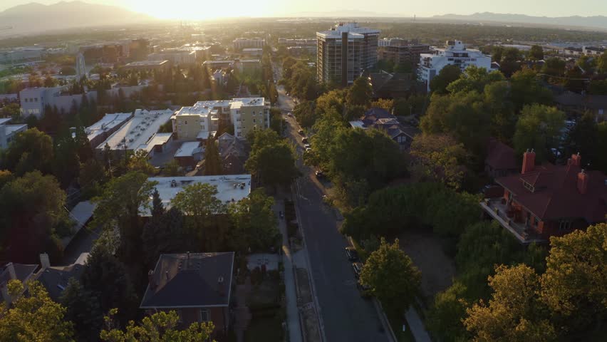 Aerial drone shot of the west Salt Lake Valley from Capital Hill, dollying in over homes, apartments, and small roads. Vibrant fall trees glow in the golden-orange hues of a colorful autumn sunset.