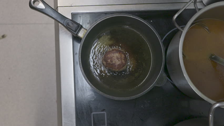 A sizzling steak rests in a hot, bubbling pan of oil on the stovetop, with a slight camera shake capturing the lively cooking process.