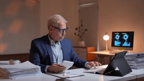 Focused mature entrepreneur sitting at desk in office at night working with calculator, digital tablet and documents, doing accounting and financial analysis - Powered by Shutterstock - Get 15% off with code: PIKWIZARD15