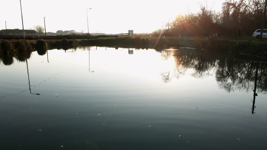 Reflections on calm water at sunset near a roadside in a tranquil rural setting
