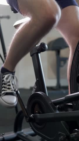 Athletic guy doing cardio workout on exercise bike. Young strong man training to be fit and healthy. Motivation and strength. Vertical video.