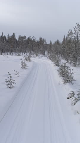 AERIAL: Flying above a car driving through slippery turn on empty snowy road in pine forest at golden winter sunrise. People on road trip traveling across snow covered Lapland wilderness at sunset