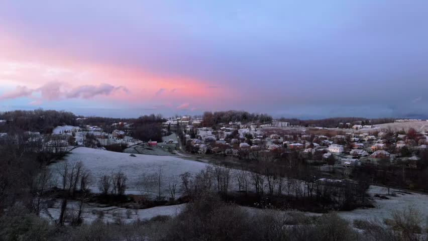 Aerial dolly over leafless forest at sunset to Morgantown, West Virginia, snowy fields and glowing horizon of quaint suburb