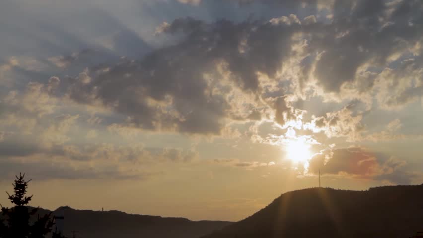 Light rays behind sky with clouds, beautiful golden sunset, mountain range, hill