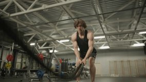 Muscular man performing battle rope double waves exercise during high-intensity workout in gym equipped with weightlifting racks. Zoom-in shot - Powered by Shutterstock - Get 15% off with code: PIKWIZARD15