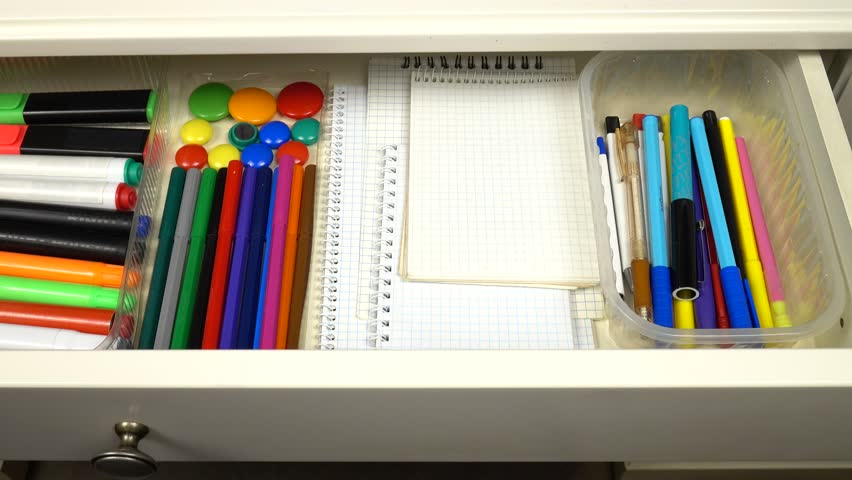 Stationery and office supplies are laid out in an open drawer of a white desk. Organizing and storing things in the house