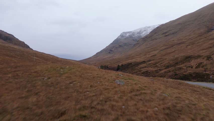 Car driving through Highlands moors, Glen Etive in Scotland, aerial tracking shot