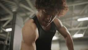 Muscular man in sportswear performing seated dumbbell one-arm curls on gym bench during bodybuilding training. Tilt-up shot - Powered by Shutterstock - Get 15% off with code: PIKWIZARD15