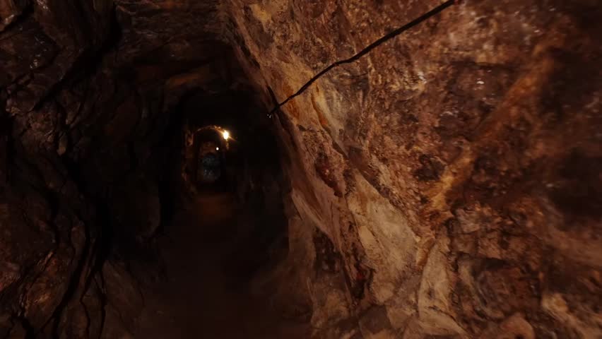 A dimly lit underground tunnel showcasing rugged rock walls, illuminated by faint lights, revealing the secrets of an ancient mine. (POV)