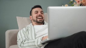 Joyful young man laughing heartily while using a laptop on a cozy sofa, enjoying a delightful moment filled with happiness and amusement in a relaxed indoor space, creating a cheerful leisure. High - Powered by Shutterstock - Get 15% off with code: PIKWIZARD15