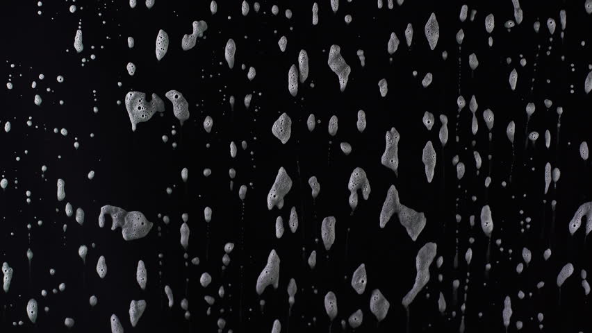 Thick foam slides gracefully down a black surface, forming dynamic patterns before dissolving. Ideal for showcasing cleaning products, transitions, or visually engaging ads.