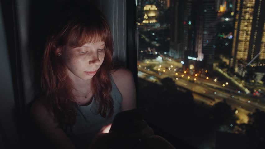 Young woman using smartphone at night by the window in kuala lumpur