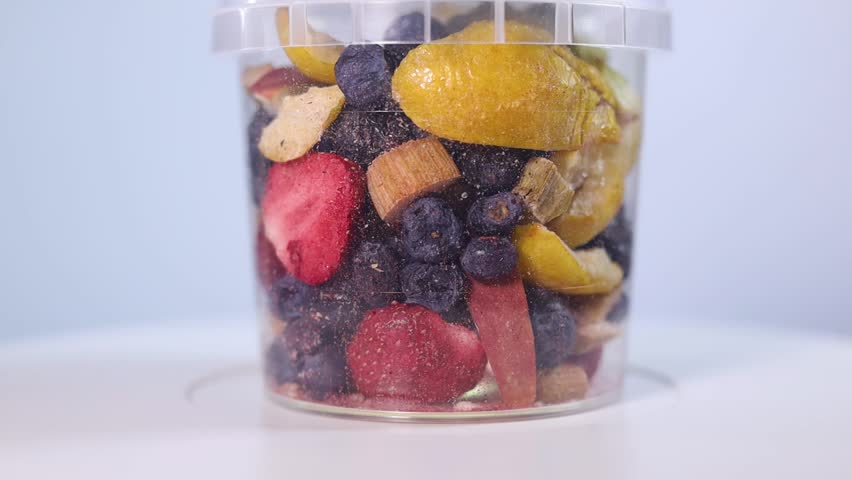 A transparent jar filled with a colorful assortment of freeze-dried fruits and vegetables, including blueberries, cranberries, raspberries, apple slices, pumpkin cubes, and more.