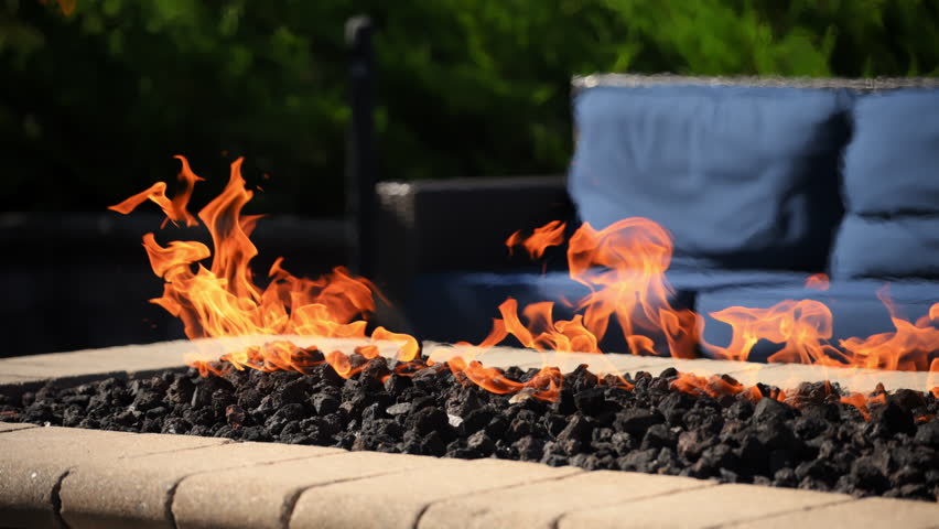 The fire pit with high flames and a comfort blue chairs on a porch. Comfort resting area with a green background.