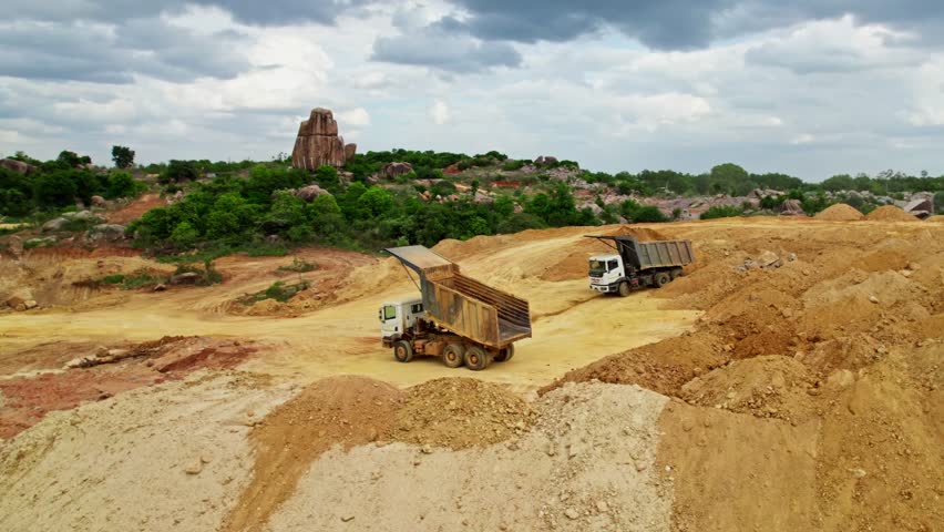 Sand dump area in construction site with trucks, trees, rocks and clouds on sky at telangana, india. day time, semi orbit, drone shot, 4k.
