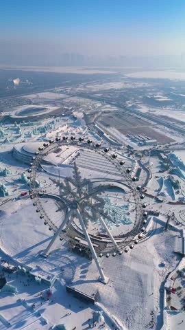 Vertical slow pull-in drone shot of the Snowflake Ferris Wheel at the Harbin Ice Festival 2025. Snowy cityscape in the background. China