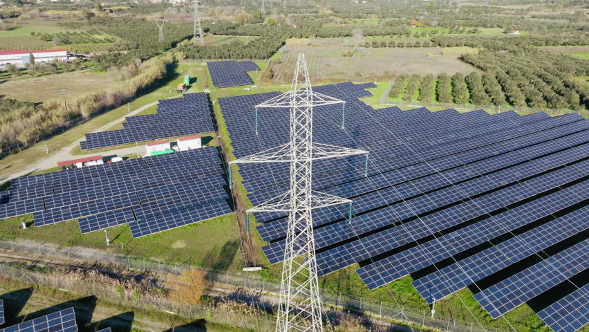 Aerial of electricity transmission tower at a solar farm, Photovoltaic power station for generating clean energy for households in a large green field with agricultural lands nearby